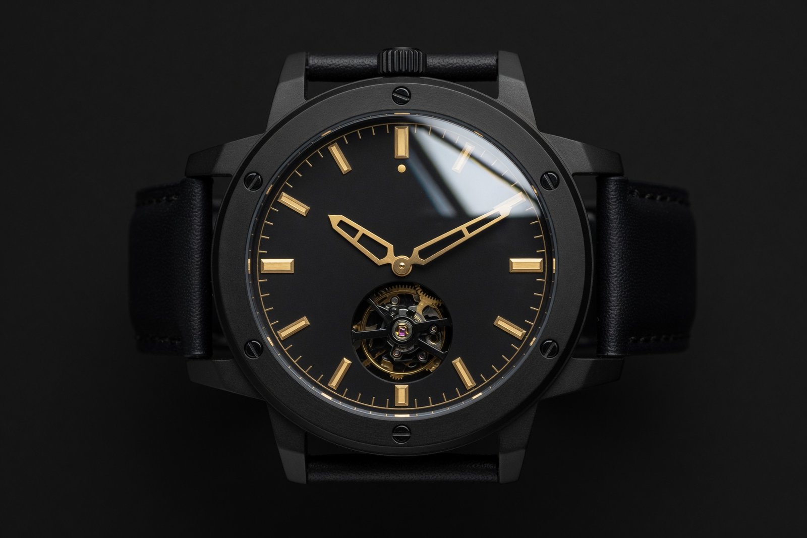 Macro photograph of a matte black luxury watch with gold hands and indices on a black background