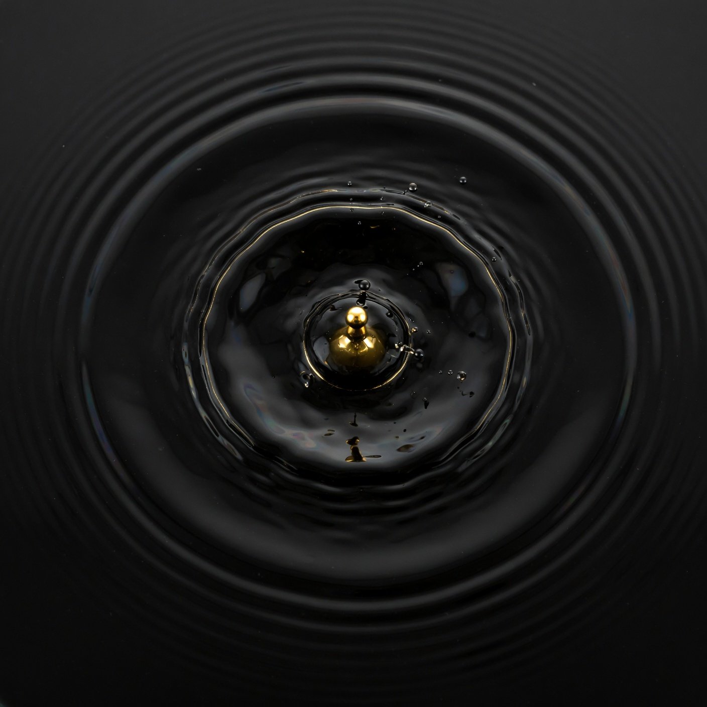 A single gold droplet suspended above rippling black water, abstract macro photograph