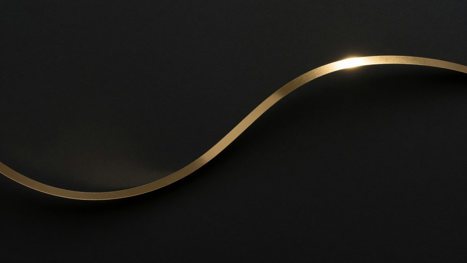 A brushed gold ribbon curving across a matte black background, abstract macro photograph